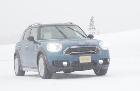 A blue Countryman driving on a snow-covered country road while it’s snowing.